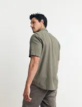 Camisa sport de manga corta color verde oliva, línea premium, con cuello clásico, cierre frontal con botones de coco y bolsillo de parche en el pecho. Confeccionada en lino y algodón.