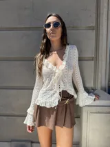 Blusa de tejido calado color crema, con escote en V, volados y lazos de ajuste en el frente, y mangas largas acampanadas.