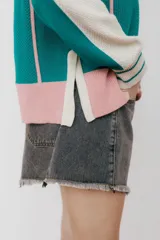 Buzo tipo polo de punto con rayas verticales en tonos beige, marrón y rosa. Tiene cuello polo marrón, cierre parcial con botones amarillos y terminaciones acanaladas en puños y ruedo.