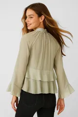Blusa color verde claro de poliéster con cuello alto fruncido, mangas largas con puños elásticos y volados en el frente.