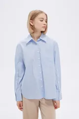 Camisa a rayas verticales verdes y blancas, de corte holgado, manga larga con puños abotonados, cuello clásico y bolsillo de parche en el pecho.