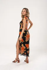 Vestido midi negro con estampado de flores naranjas y beige, espalda descubierta con tres botones en forma de flor, tajo lateral y flecos en el ruedo.