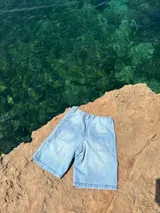 Short de jean celeste con bolsillos delanteros y traseros, y estampado con el logo de la marca en la pierna izquierda.