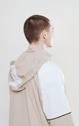 Anorak unisex beige y blanco con capucha, cierre parcial con cremallera, bolsillo tipo canguro con solapa y cordones ajustables con texto en la capucha.