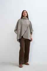 Ruana color gris con cuello alto, cierre cruzado con broche y bolsillos laterales. Terminaciones envivadas. Prenda oversize sin forro confeccionada en lana fina.