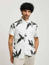 Camisa blanca estampada con hojas en tonos de verde y gris, de corte recto, manga corta y cuello clásico.