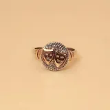 Anillo plateado con apliques dorados, con diseño de máscaras de teatro en el centro.