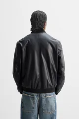 Cazadora bomber negra de efecto piel, corte relaxed fit, con cuello y puños de rib elástico, cierre frontal con cremallera, bolsillos laterales de doble vivo y bolsillo interior.