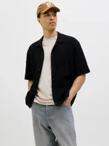 Polo negro de tejido cable knit con fit relajado, cuello tipo polo, manga corta y cierre con botones.