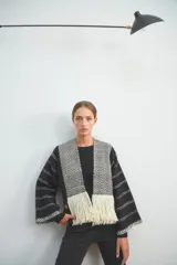 Chaqueta de punto en color negro con detalles en blanco, de frente abierto y diseño holgado. Presenta paneles frontales con patrón de zigzag y terminación de flecos en el ruedo, mientras que las mangas exhiben un motivo de líneas punteadas horizontales.