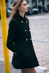 Abrigo negro de lana con cuello subido, manga larga, bolsillos delanteros de vivo y cierre frontal cruzado con botones dorados.