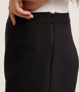 Short pollera negro ajustado, confeccionado en tejido plano de estructura sastre, con pences, cierre lateral por cremallera invisible y mini bolsillos delanteros.