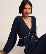Blusa de mangas largas color azul marino, confeccionada en viscolino con 30% de lino, con escote V, lazo en el cuello con punta y bieses contrastantes luego abajo del escote, además del bajo de volado.