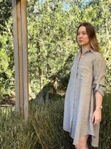 Vestido camisero blanco de lino, con cuello camisero, manga larga con botón para recoger, cierre frontal con botones de nácar, bolsillo en el pecho y diseño asimétrico más largo en la parte trasera.