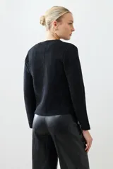 Chaqueta tejida negra con cuello redondo, cierre frontal con botones dorados, bolsillos delanteros y corte clásico.