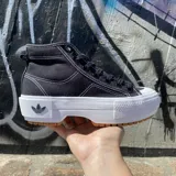 Zapatillas Adidas Nizza Trek de caña alta, color negro con costuras blancas contrastantes. Presentan suela de goma blanca con detalles en marrón y logo de Adidas en la lengüeta y el lateral.
