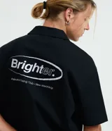 Camisa boxy de algodón texturizado color negro, con cuello bowling, manga corta y cierre abotonado. Presenta bordados en el frente y la espalda.