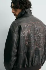 Cazadora bomber de piel color marrón oscuro envejecido, con cuello solapa, cierre frontal de cremallera y puños y bajo en rib elástico. Presenta grabados en relieve en el delantero y la espalda.