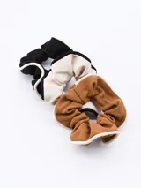 Set de tres scrunchies de tela acanalada en colores negro, beige y marrón, con borde blanco.