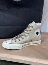 Zapatilla de lona color beige, de caña alta y acordonada. Tiene suela y puntera de goma color blanco y logo de Peach en el lateral.