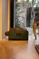 Neceser de lona verde con detalles en cuero color beige y etiqueta con logo de la marca Sierra Mora.