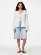 Blusa blanca de algodón con escote en V y mangas largas abullonadas. Presenta cierre frontal con lazos.