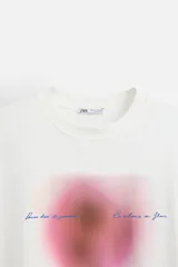 Camiseta blanca de corte relaxed fit, cuello redondo y manga corta. Estampado combinado a contraste en el delantero con imagen borrosa de flor y texto en azul.