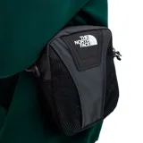 Bandolera negra de poliéster con detalles en cuero sintético. Tiene correa ajustable, cierre superior con cremallera, bolsillos internos y gancho para llaves. El logo de The North Face está estampado en blanco en el frente.