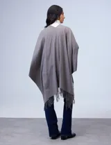 Ruana de tejido suave color negro con terminación en flecos, diseñada para un look cómodo y elegante.