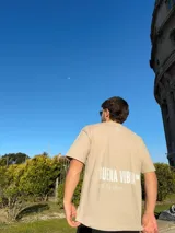Remera color beige de corte semi oversize con estampa blanca en la espalda con la frase "Buena Vibra" y "feel the vibes".