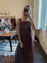 Vestido largo color marrón oscuro, con escote cuadrado y tirantes anchos. Presenta un ribete contrastante en color camel a lo largo de los laterales y un monograma bordado en el pecho.