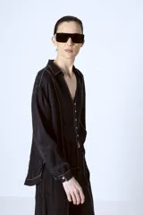 Blusa negra con botones, cuello camisero y mangas largas con puños. Presenta pespuntes blancos en contraste.
