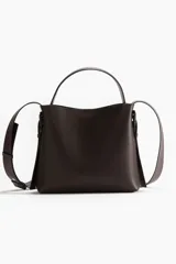 Cartera bandolera de cuero sintético color marrón oscuro, con asa corta superior y correa larga ajustable. Tiene dos compartimentos con cierre magnético y forro interior.