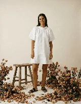 Vestido blanco de lino 100%, manga corta ranglan abuchonada, calce holgado evasé con volado y acceso trasero con botón forrado en lino.