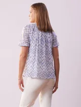 Blusa de microtul estampada con diseño zigzag en tonos celeste y blanco, de la marca Cable & Gauge. Tiene cuello a la base con escote en V y lazo de ajuste, mangas cortas con puño elastizado y forro interno a tono.