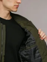 Campera bomber Calvin Klein color verde militar con diseño acolchado en forma de rombos. Tiene cierre frontal con cremallera, cuello, puños y dobladillo acanalados, bolsillos laterales y un bolsillo con cremallera en la manga izquierda con el logo de la marca.