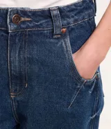 Pantalón mom confeccionado en jeans azul con trabillas en la cintura, cierre tradicional por botón y cremallera, bolsillos delanteros y traseros con detalle deshilachado.