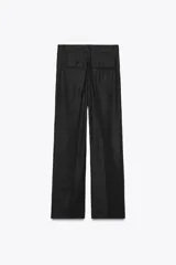 Pantalón negro de tiro medio con trabillas, pliegues frontales, bolsillos laterales y falsos bolsillos de vivo en la espalda. Cierre frontal con cremallera y botón.