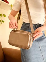 Bandolera color visón, fabricada en cuero con forro de tela. Tiene bolsillo interior y exterior. Entra billetera grande.