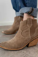 Bota corta de gamuza color marrón oscuro, con puntera cuadrada y detalles de costuras decorativas. Tiene un taco de madera con forma cónica.