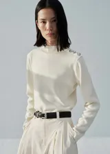 Jersey color crudo de punto fino con cuello perkins, manga larga y detalle de botones metálicos en el hombro. Corte recto.