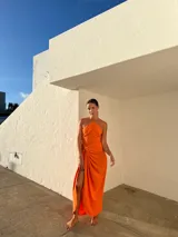 Vestido largo naranja de crepé con escote halter y falda tipo pareo con abertura lateral.