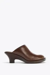Zueco de cuero color marrón con tacón de 6 cm y detalle elástico lateral.