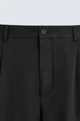 Pantalón negro de corte recto confeccionado en tejido de algodón con elasticidad. Presenta pliegues en la parte delantera, bolsillos laterales y traseros de vivo. Cierre frontal con cremallera y botón.