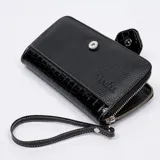 Billetera dorada con cierre metálico y solapa con el logo de la marca Vanitas. Tiene múltiples compartimentos para tarjetas y billetes. Incluye correa de muñeca extraíble.