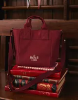 Cartera mini de lona color crudo con estampado "The Brunch Club" en azul marino. Tiene correa regulable y desmontable, manijas superiores y cierre superior.