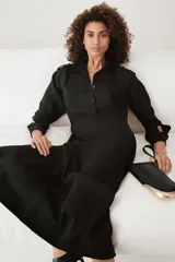 Vestido largo negro tipo camisero, confeccionado en viscosa. Tiene cuello solapa, manga larga con puños, bolsillos delanteros y cierre frontal con botones. Incluye cinturón ajustable con trabillas y botones.