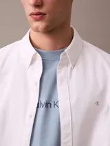 Camisa blanca de manga larga, confeccionada en tejido Oxford de algodón y elastano. Tiene cuello abotonado, cierre frontal con botones y logo de Calvin Klein bordado en el pecho. Corte regular.