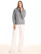 Buzo de punto grueso color beige, con cuello volcado y textura en relieve. Tiene mangas largas de corte hombro caído y puños anchos.