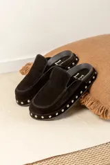 Zuecos de gamuza color marrón chocolate, con base de goma negra, tachas plateadas alrededor de la base y plantilla acolchada.